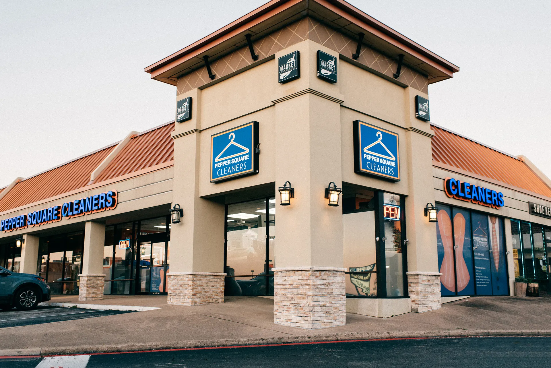 A dry cleaners storefront in a shopping center with blue "Pepper Square Cleaners" signs and large windows.