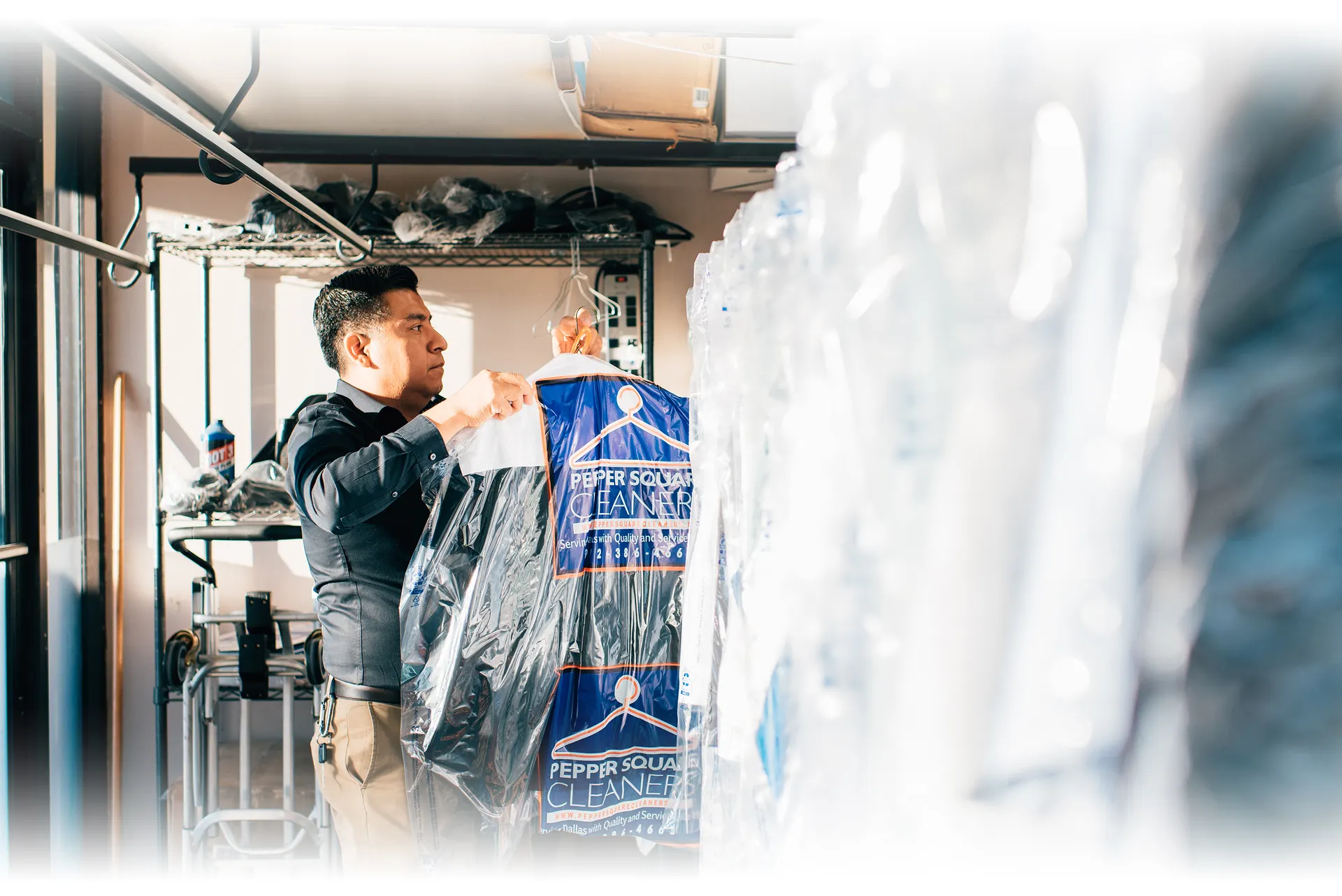A man arranges plastic-covered clothes on racks at a dry cleaning business.