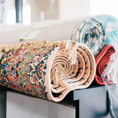 Several rolled-up area rugs with intricate patterns rest on a black table, with one rug partially wrapped in plastic.